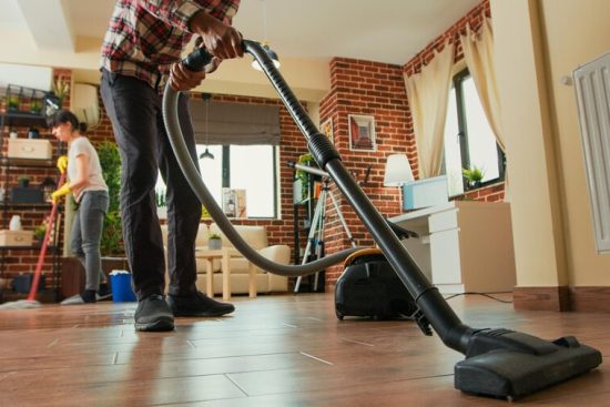 african-american-man-vacuuming-floors-living-room-cleaning-apartment-with-girlfriend-young-adult-using-vacuum-cleaner-woman-wiping-shelves-with-all-purpose-cleaner-tripod-shot_482257-64035