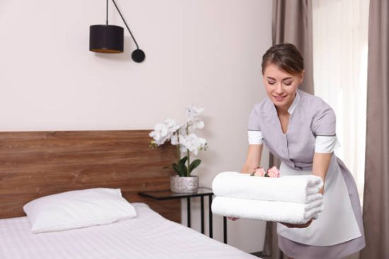 beautiful-chambermaid-putting-fresh-towels-on-bed-in-hotel-room