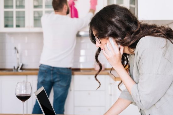 woman-using-laptop-while-man-cleaning_23-2147766964