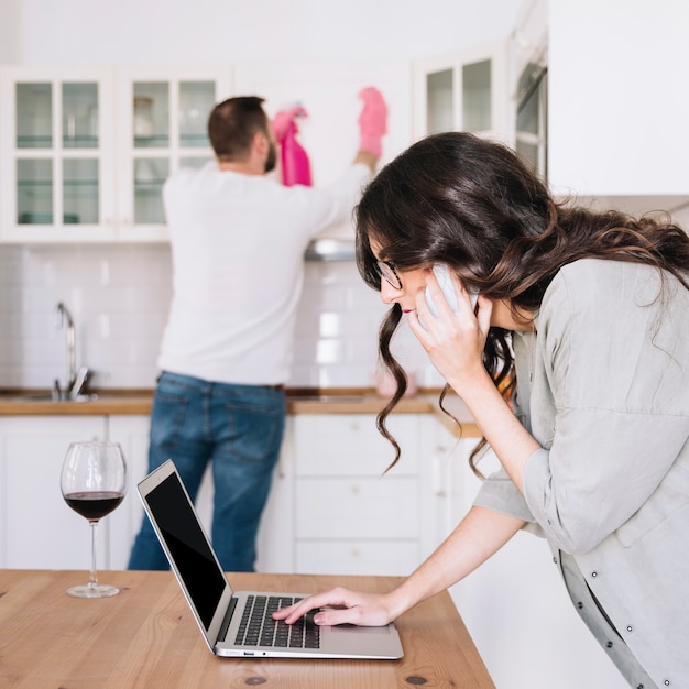 woman-using-laptop-while-man-cleaning_23-2147766964