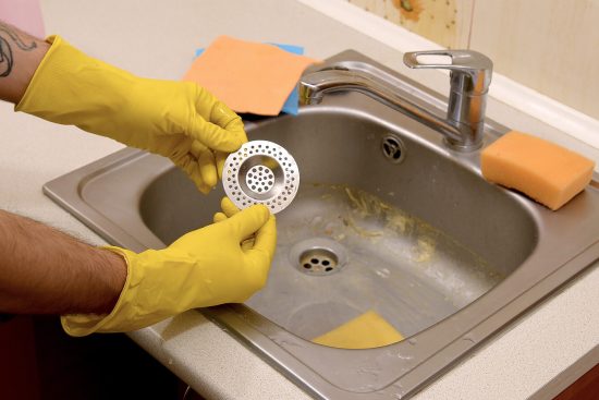 Cleaner-In-Rubber-Gloves-Shows-Clean-Plughole-Protector-of-a-Kitchen-Sink-edited